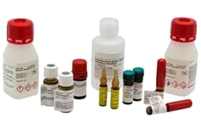 Certified Reference Materials A collection of various chemical bottles and containers with different sizes, shapes, and colors. Some bottles have red caps and labels with hazard symbols indicating flammable and corrosive substances. There are also small vials with yellow liquid, alongside tubes with white caps.