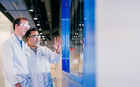 <p>值得一走的旅程--流程变更管理的便捷之路</p> Two laboratory technicians in white lab coats are engaged in a discussion while looking at a large display screen. One technician is gesturing with their hand, indicating a point of interest, while the other is attentively listening.