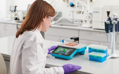 Scientist sitting at bench, looking at Millicell® DCI screen showing confluency mask of cell culture in T-75 flask Scientist sitting at bench, looking at Millicell® DCI screen showing confluency mask of cell culture in T-75 flask