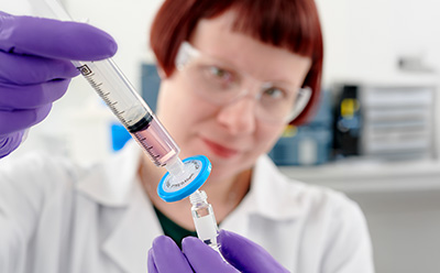 Millex syringe filter in-use Photograph of a scientist using a hydrophilic PTFE Millex® syringe filter to filter a sample into a glass vial.
