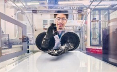 Solid electrolyte R&D A scientist wearing safety goggles and a lab coat is working inside a glove box in a high-tech laboratory. The researcher is using gloved hands through the glove ports to handle a material inside the controlled environment. The background showcases advanced lab equipment and an industrial setting, emphasizing precision and safety in handling sensitive materials
