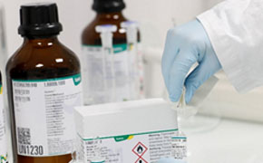 Karl Fischer Reagents & Standards The image depicts a person in a lab coat and gloves handling chemical bottles and a box with a hazard label on a laboratory counter, suggesting a safety-conscious environment.