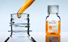 图片描述的是一个精确的科学程序，使用移液管将一滴透明液体滴入一个开口的小玻璃容器中。