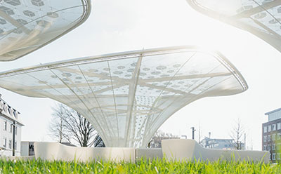 A futuristic outdoor scene with curved white solar canopy structures and solar panels, set against a bright sky and surrounding greenery.