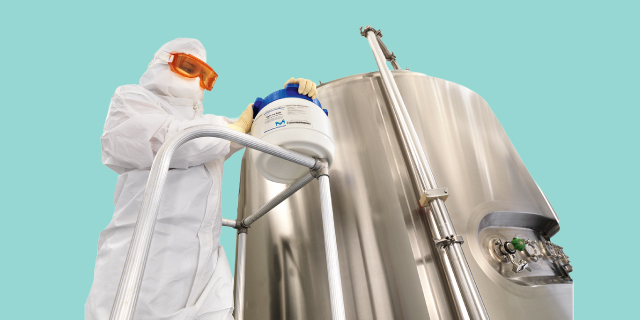 <p>Selecting the Right Media for Your Aseptic Process Simulations</p>
Cleanroom worker in protective clothing and orange goggles operates a hose beside a large stainless-steel process vessel.