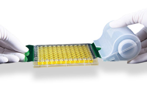 Excel Scientific Products Photograph showing two gloved hands using an adhesive seal on a roller to seal a microplate.