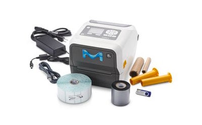MilliSentials™ Lab Labeling System 便携式小型标签打印机,机身为白色和灰色相间,正面印有蓝色 "M "标志。与打印机配套的还有各种配件,包括一个带电缆的电源适配器、三个类似墨水卷的圆柱形物体(颜色分别为黄色和黑色)、一个蓝色塑料小部件(似乎是打印机机械装置的一部分)和一卷标签。
