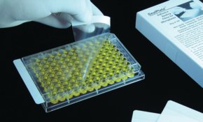 A person wearing white gloves handling a SealPlate® film, with a white box and paper nearby,