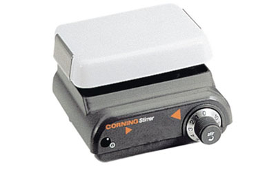 A Corning Stirrer, a laboratory equipment with a white top and grey base, equipped with control knobs and labeled ‘CORNING Stirrer’, designed for mixing solutions in a lab setting.