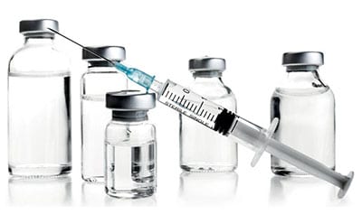 一支带针头的医用注射器，内含部分液体，斜置于五支不同尺寸、带金属盖的药瓶前方，背景为纯白色。