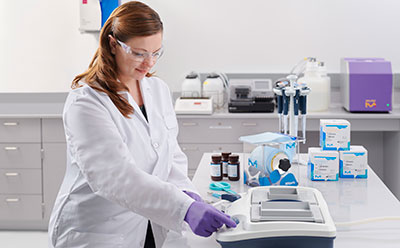 Western blotting using the SNAP i.d.® 2.0 protein detection system A professional in a lab coat and purple gloves working with a Membrane Immunodetection device in a well-equipped laboratory, surrounded by various laboratory equipment and supplies, highlighting the precision and care involved in immunodetection processes.