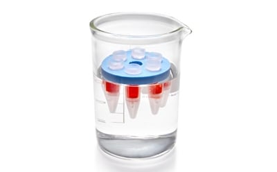 D-Tube™ 透析器 一个透明的实验室烧杯中装满了无色液体,里面放着一个装有红色液体的圆柱形小容器。该容器顶部盖着一个蓝色盖子,漂浮在烧杯液体的表面上。烧杯侧面有刻度线,标明了其容量。