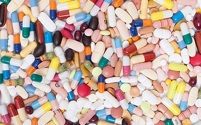 The image displays a close-up view of a diverse assortment of colorful pills and capsules, varying in shape and size, densely packed to fill the entire frame without any visible branding or text.