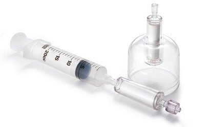 该图像似乎是一个医疗或实验室装置，其特点是一个注射器与一个带瓶塞和出口的玻璃瓶相连。注射器上有测量标记，玻璃瓶类似于科学实验室中用于储存化学品或溶液的试剂瓶。
