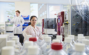 Analytical Development Services One male and one female scientist working in an analytical development lab for biologics preparing and analyzing samples with many bottles with white and red caps.
