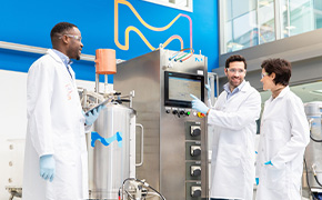 Upstream Processing (USP) for mAbs Three scientists stand next to a bioreactor.
