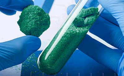 High purity green powder precursor for cathode material preparation. Green crystalline powder inside a test tube, shown as an example of high purity metal salts used in battery cathode synthesis.