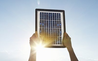 Solar cell panel held against the sky during illumination. Solar cell module raised against bright sunlight, showing photovoltaic material in use.