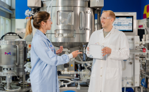 Ensure compliant and deliverable URS Two team members discussing requirements near downstream processing equipment in a biopharmaceutical manufacturing facility.