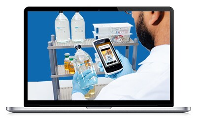M Trace Webinar A person in a white lab coat holding a smartphone while observing a cart with various laboratory bottles against a blue backdrop.