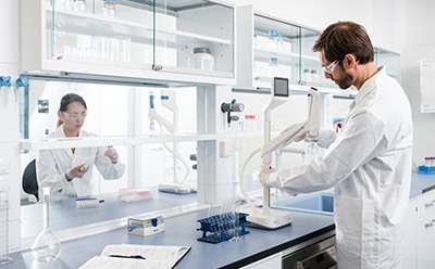 实验室场景：两名身着白色实验服的科学家正在操作实验设备，包括两台Q-POD超纯水分配器及各类玻璃器皿。