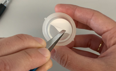 Swinnex<sup>®</sup> Filter Placement Photograph of a person’s hands using forceps to place the cut disc filter