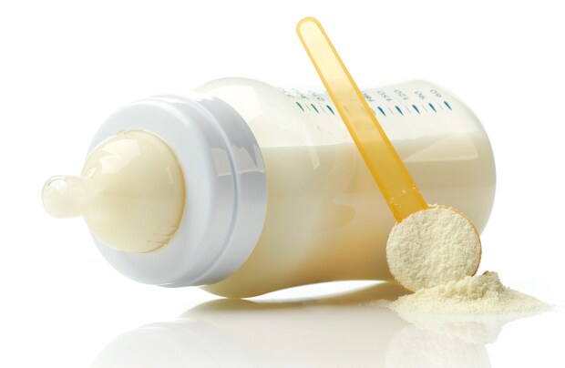 A baby bottle filled with milk, accompanied by a yellow measuring scoop and powdered formula on a white surface