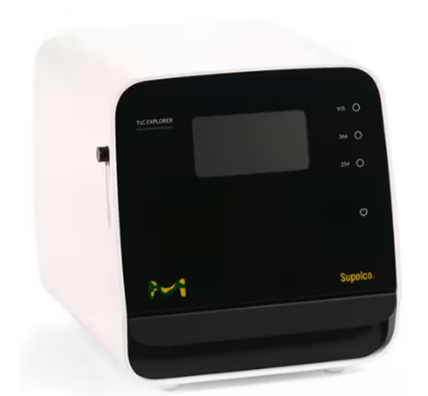 A compact laboratory instrument, TLC Explorer, with a white body and a glossy black front panel. The front features a rectangular screen in the upper center, likely used for displaying readings or navigation menus. To the right of the screen are three vertically aligned indicator labels marked “VIS,” “365,” and “254,” corresponding to different light wavelengths used for TLC plate visualization. Below the screen, the black surface includes a bright green and yellow Merck logo on the left and the brand name “Supelco” in yellow on the right. The left side of the device has a small protruding switch or button. The overall design is sleek and minimalistic, with the device sitting on a white surface, suggesting it is ready for benchtop use in an analytical laboratory setting.