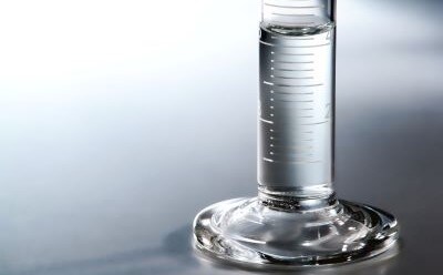 Graduated cylinder made of glass filled with 40 mL of water on a white and grey background​