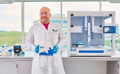 Scientist with ELISA Kit In Front of AAW™ Workstation Smiling male scientist standing in front of AAW™ automated assay workstation holding ELISA kit with automated protocol.