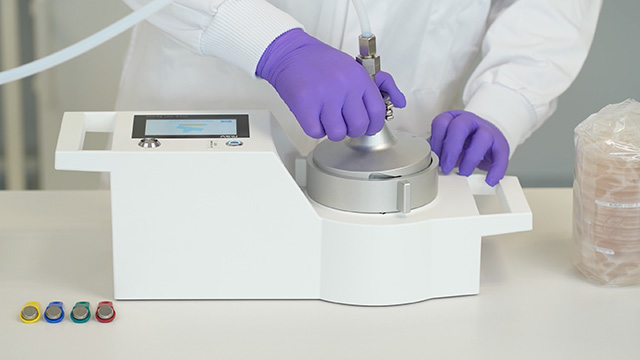 <p>MAS-100 Atmos<sup>®</sup> microbial compressed gas sampler</p>
Close-up of purple-gloved hands operating a microbial compressed-gas sampler on a laboratory instrument.