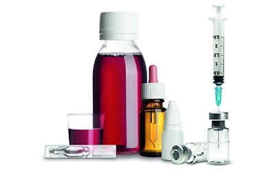 From left to right, the image shows a cup with a red liquid, a glass container of the same red liquid, a brown glass vial with a dropper for a lid, a plastic bottle of eye drops, a glass vial lying on its side, and a glass vial containing a clear liquid with a syringe inserted at the top.