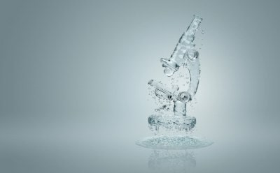 A transparent glass microscope with water droplets suspended in mid-air set against a aqua background.