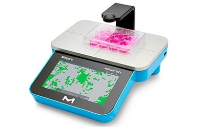 Photograph of the Millicell® DCI Digital cell imager for measuring confluency and cell count, with plate of hanging cell culture inserts in 24-well format on platform Photograph of the Millicell® DCI Digital cell imager for measuring confluency and cell count, with plate of hanging cell culture inserts in 24-well format on platform