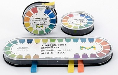 Three containers of pH indicator paper strips, each with a color-coded pH range chart on the lids. The containers are cylindrical, with one lying horizontally and two stacked vertically, all shown against a white background. Each container also has a small piece of tape in various colors to presumably mark different pH ranges. Three containers of pH indicator paper strips, each with a color-coded pH range chart on the lids. The containers are cylindrical, with one lying horizontally and two stacked vertically, all shown against a white background. Each container also has a small piece of tape in various colors to presumably mark different pH ranges.