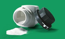 一个被打翻的白色补充剂瓶子，黑色瓶盖脱落，躺在旁边。一堆白色粉末从瓶子里洒落在绿色的表面上。