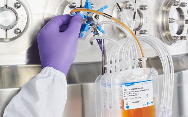Sterile and Aseptic Sampling Solutions Hands of a person in a labcoat and gloves working with a sampling system attached to a stainless steel bioreactor.