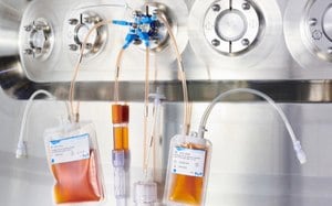 NovaSeptum® GO Sampling Systems for multi-use processes in biopharmaceutical manufacturing Sampling manifold with multiple different containers connected to a stainless steel bioreactor via tubing and a blue and white holder. Containers include bags, a syringe, a bottle, and a tube with samples in orange-colored cell culture medium