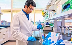 Scientist in a lab coat working at a laboratory bench, surrounded by various laboratory equipment and materials.