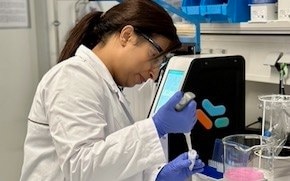 Aditi正佩戴着防护装备，用移液管在实验室中提取溶液。