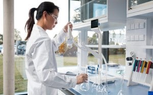 Female scientist in a white lab coat is filling volumetric flasks with ultrapure water from a Q-POD dispenser in a modern lab setting with a bright and organized workspace