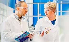One scientist explaining new innovation to another scientist in front of a blue window.