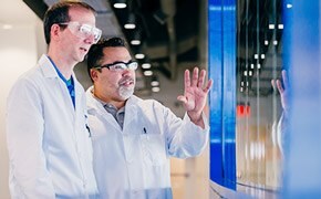 Two scientists discussing innovations One scientist explaining new innovation to another scientist in front of a blue window