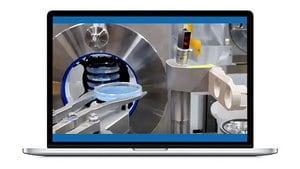 制造车间内机械组件的特写镜头，机械臂正在处理一个圆形蓝色部件。背景中可见闪亮的金属表面和圆形开口，暗示着高科技环境。该场景显示在笔记本电脑屏幕上。