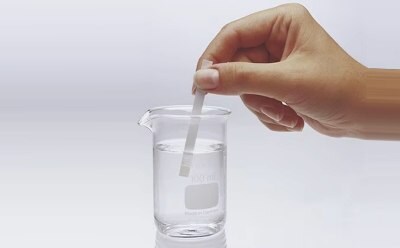 Chemist dips MQuant® test strip in a liquid contained in a small beaker to test a chemical parameter