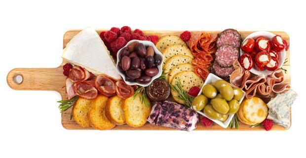 Charcuterie board with a selection of savory snacks and preserved foods. Displayed on a charming wooden board equipped with a convenient handle, the charcuterie platter presents a delightful assortment of savory delicacies. The carefully curated selection includes a variety of preserved meats, enticing olives, flavorful peppers, luscious berries, crisp crackers, and an array of delectable cheeses.