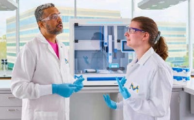 Two scientists standing in front of AAW™ automated assay workstation having a conversation.