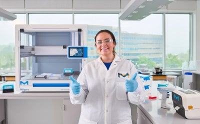 Female scientist standing in front of AAW™ automated assay workstation smiling and giving double thumbs up.